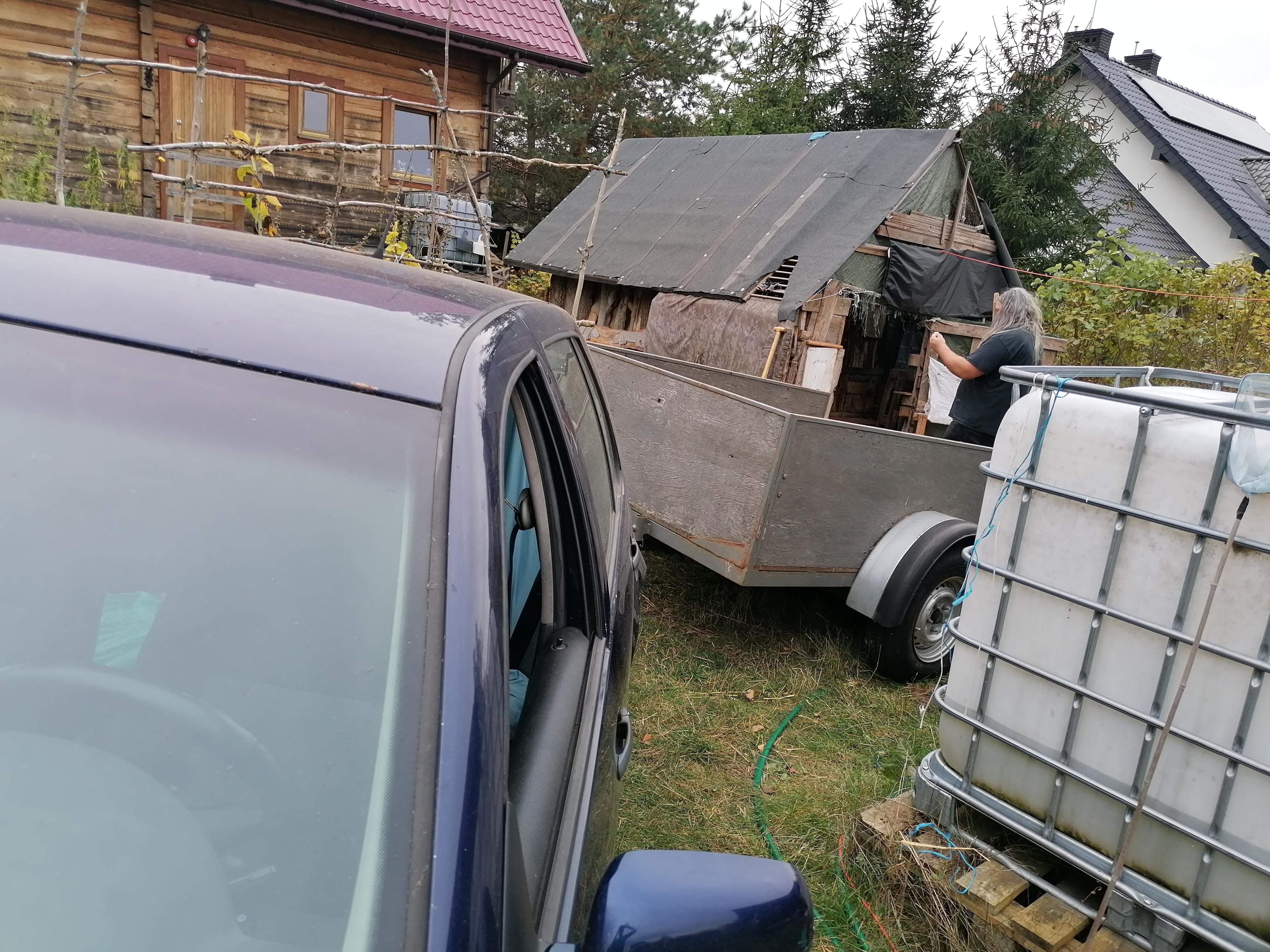 auto z przyczepą wśród zabudowań gospodarskich- na przyczepę ładowany jest obornik