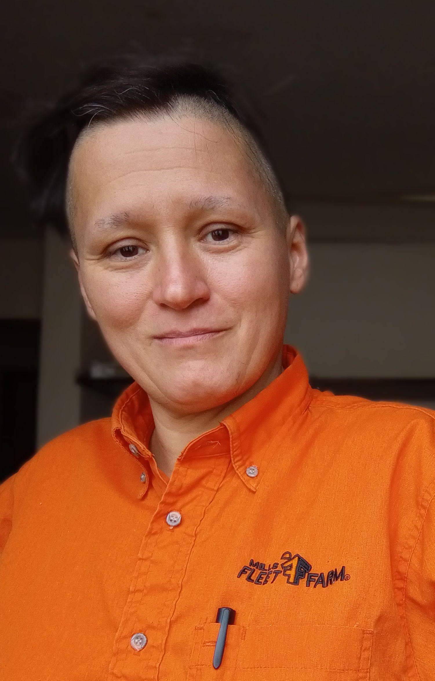 Postać z wygolonymi bokami głowy i w pomarańczowej koszuli roboczej